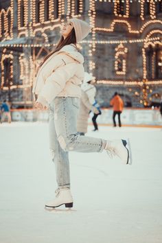 a woman skating on an ice rink in front of a large building with christmas lights