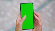 a person holding a cell phone with a green screen in their left hand while looking at the camera