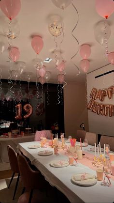 a birthday party with pink balloons and streamers hanging from the ceiling over a long table