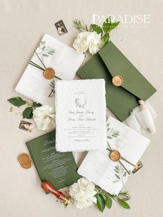 the wedding stationery is laid out on top of white flowers and green envelopes