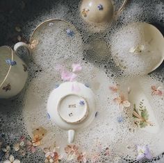 tea cups and saucers sitting on top of a table covered in water droplets with flowers