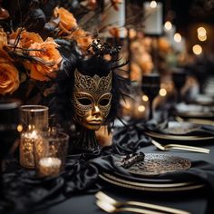 a table set with black and gold dinnerware, candles and a masquerade mask