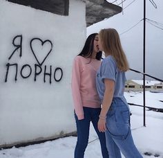 two young women standing next to each other in front of a building with graffiti on it