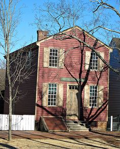 an old red house with white picket fence and trees in the foreground, on a sunny day