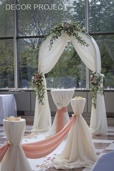 an arch decorated with flowers and greenery for a wedding ceremony in front of large windows