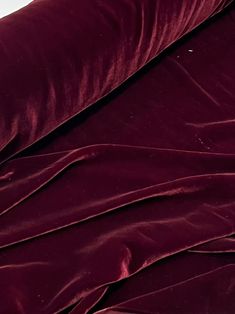 a cat laying on top of a bed covered in a maroon comforter and pillows