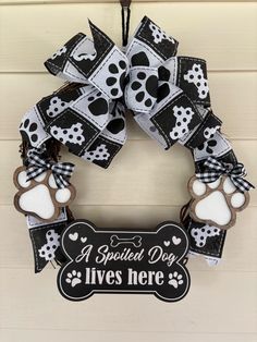 a black and white dog's paw print wreath hangs on a door with a sign that says, a spoiled dog lives here