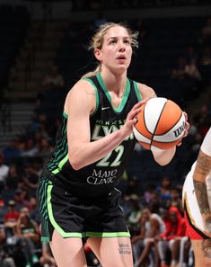 a woman holding a basketball in her right hand while standing next to another person on a court