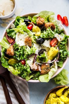 a salad in a bowl with olives, tomatoes and bread croutons on the side