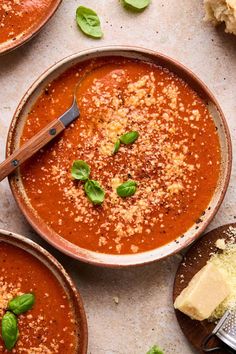 two bowls of tomato soup with basil and parmesan cheese on the side next to bread