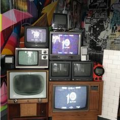 several televisions are stacked on top of each other in front of a wall with graffiti