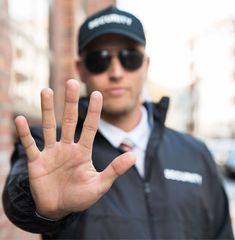 a man wearing sunglasses and a black jacket holds his hand up in front of him