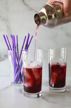 someone pouring red liquid into two glasses with purple straws in them and another glass filled with ice