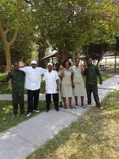 a group of people standing next to each other on a sidewalk near trees and grass