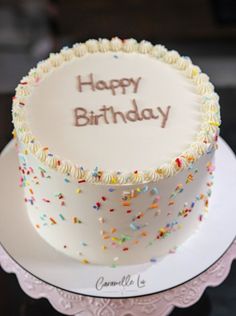 a white birthday cake with sprinkles and the words happy birthday written on it