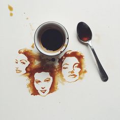 a cup of coffee and spoon sitting on top of a white surface with the faces of three women painted on it