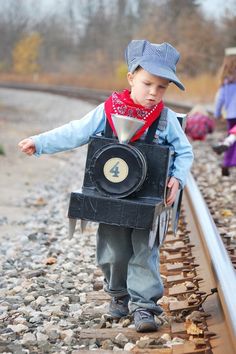 a little boy that is standing on some train tracks with a box in his hand