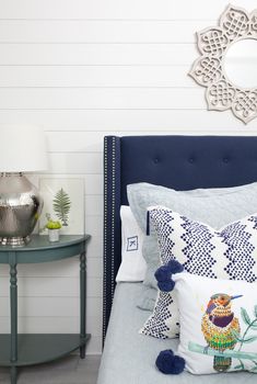 a bed with blue and white pillows on top of it next to a night stand