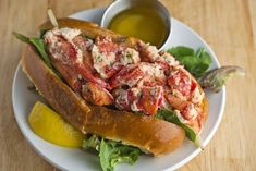 a lobster sandwich on a roll with lettuce and lemon wedges