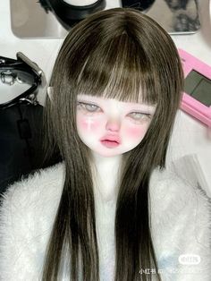 a close up of a doll with long hair near other dolls and makeup brushes on a table