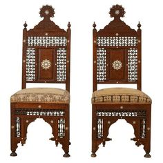 a pair of carved wooden chairs with patterned upholstered back and seat cushiones