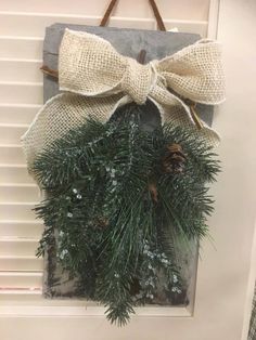 a wreath hanging on the front door with pine cones and burlocks tied to it