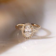 an oval shaped diamond ring with two halos on the side, sitting on a white surface