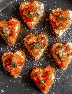 heart shaped pastries with tomatoes and herbs on a black plate covered in powdered sugar