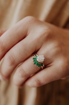 a woman's hand wearing a ring with flowers on the middle and green leaves