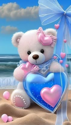 a white teddy bear holding a blue heart on the beach with pink hearts around it