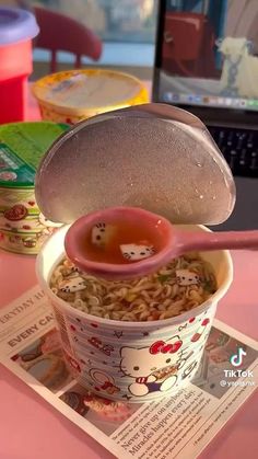 the bowl is full of noodles and has a pink spoon sticking out of it with dices in it