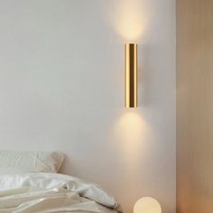 a white bed sitting next to a wall mounted light on the side of a wall