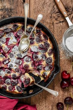 a cherry cobble cake in a cast iron skillet next to cherries and sugar