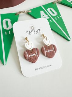 a pair of earrings with a football and heart on it sitting next to a green pennant