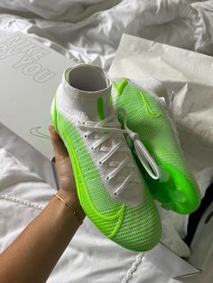 a person holding up a pair of neon green shoes on top of a white bed