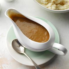 a bowl of gravy on a plate next to mashed potatoes