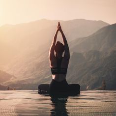 a woman doing yoga in the middle of a pool with mountains in the back ground