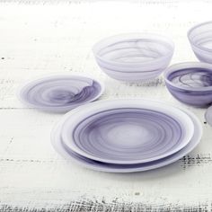 four purple glass bowls sitting on top of a white table next to two empty plates