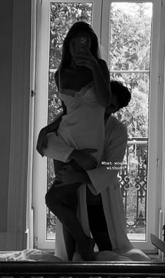 black and white photograph of a woman holding a child in front of a window, taking a selfie with her cell phone