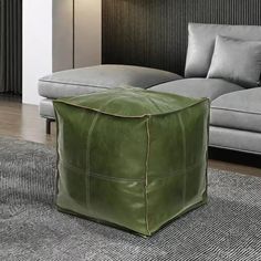 a green leather ottoman sitting on top of a rug in front of a gray couch