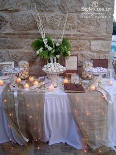 a table topped with lots of desserts next to a stone wall covered in lights