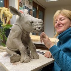 a woman standing next to a statue of a rhino and a baby rhinoceros