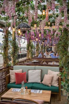 an outdoor seating area with wicker furniture and flowers hanging from the ceiling above it