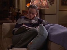 a young boy sitting on top of a couch next to a lamp and pillow in a living room