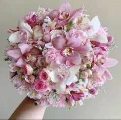 a bridal bouquet with pink and white flowers in someone's hand on a gray background