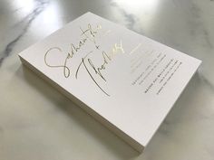 a white card with gold writing on it sitting on a counter top next to a bottle of wine