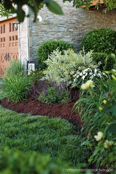 a garden with lots of green grass and flowers next to a brick building in the background