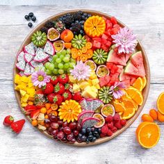 a platter filled with fruits and flowers on top of a white wooden table next to sliced oranges