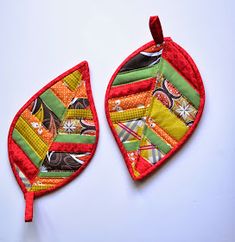 two pieces of colorful fabric hanging from strings on a white surface with one leaf shaped like an ornament