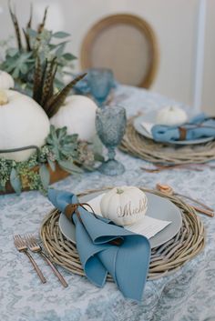 the table is set with white pumpkins and blue napkins